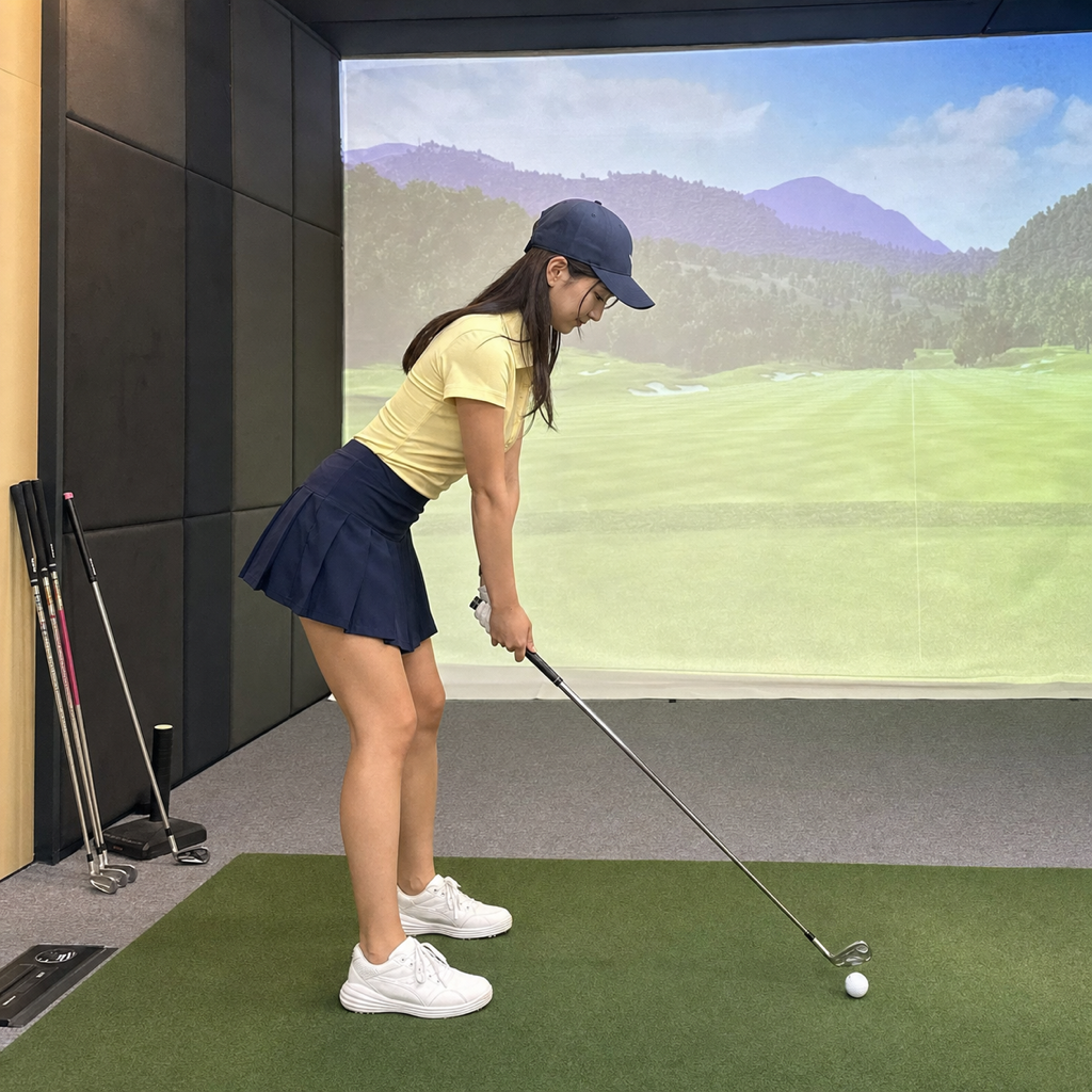 アドレスで股関節から前傾をつくる若い女性ゴルファー、屋内ゴルフシミュレーター